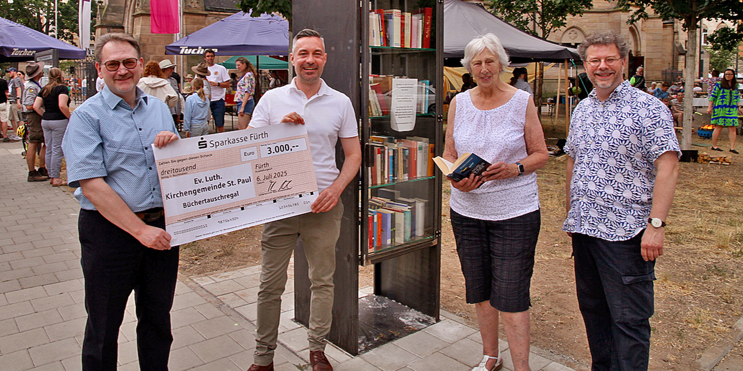 Das Büchertauschregal, das bereits wenige Tage nach seiner Aufstellung regen Zuspruch findet, wurde am Sonntag, den 6. Juli, eingeweiht. Scheckübergabe vor der Paulskirche