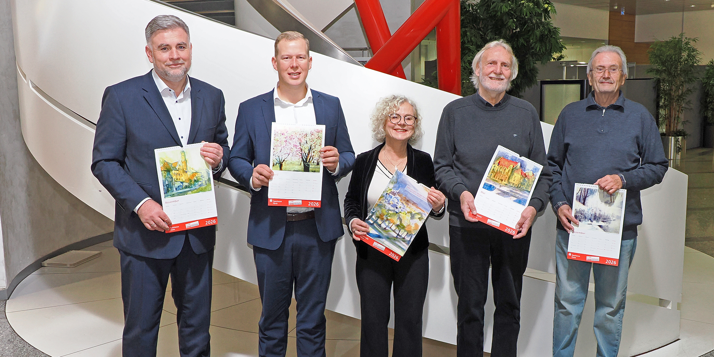 „Stadt und Land – ein Spiel mit Licht und Farbe“: Unter diesem Titel präsentiert die Sparkasse Fürth ihren Familienkalender für 2026.  v.l.n.r. John Hammond, ArtAgency – vermittelnde Künstleragentur; Kai Tusak, Mitglied des Vorstands der Sparkasse Fürth; Ilse Feiner, Künstlerin; Susanne Weimann-Kothe, Grafikerin; Adolf Dodenhöft, Vorstandsvorsitzender der Sparkasse Fürth